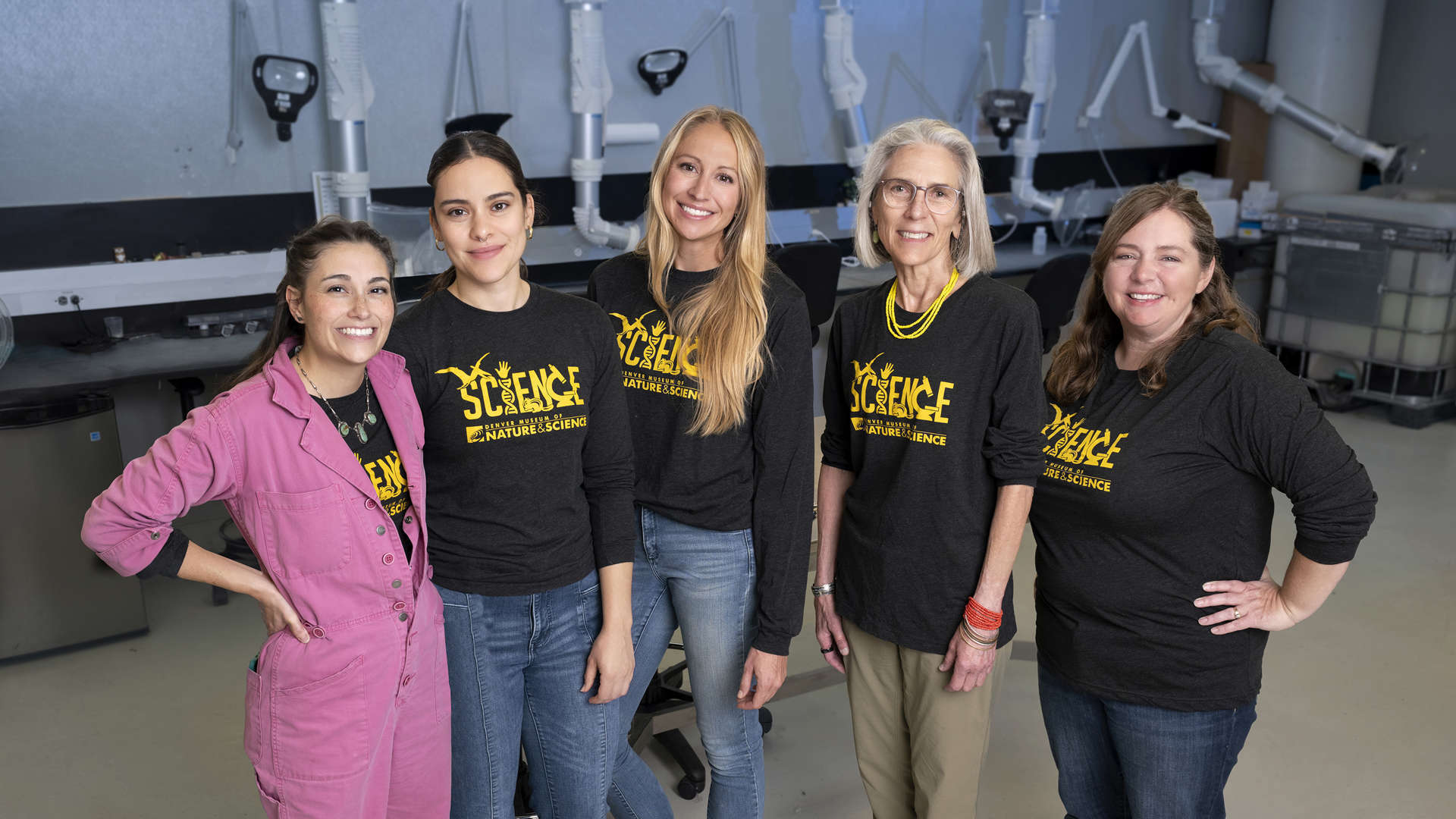 Five women in black Science shirts stand in a line in a lab