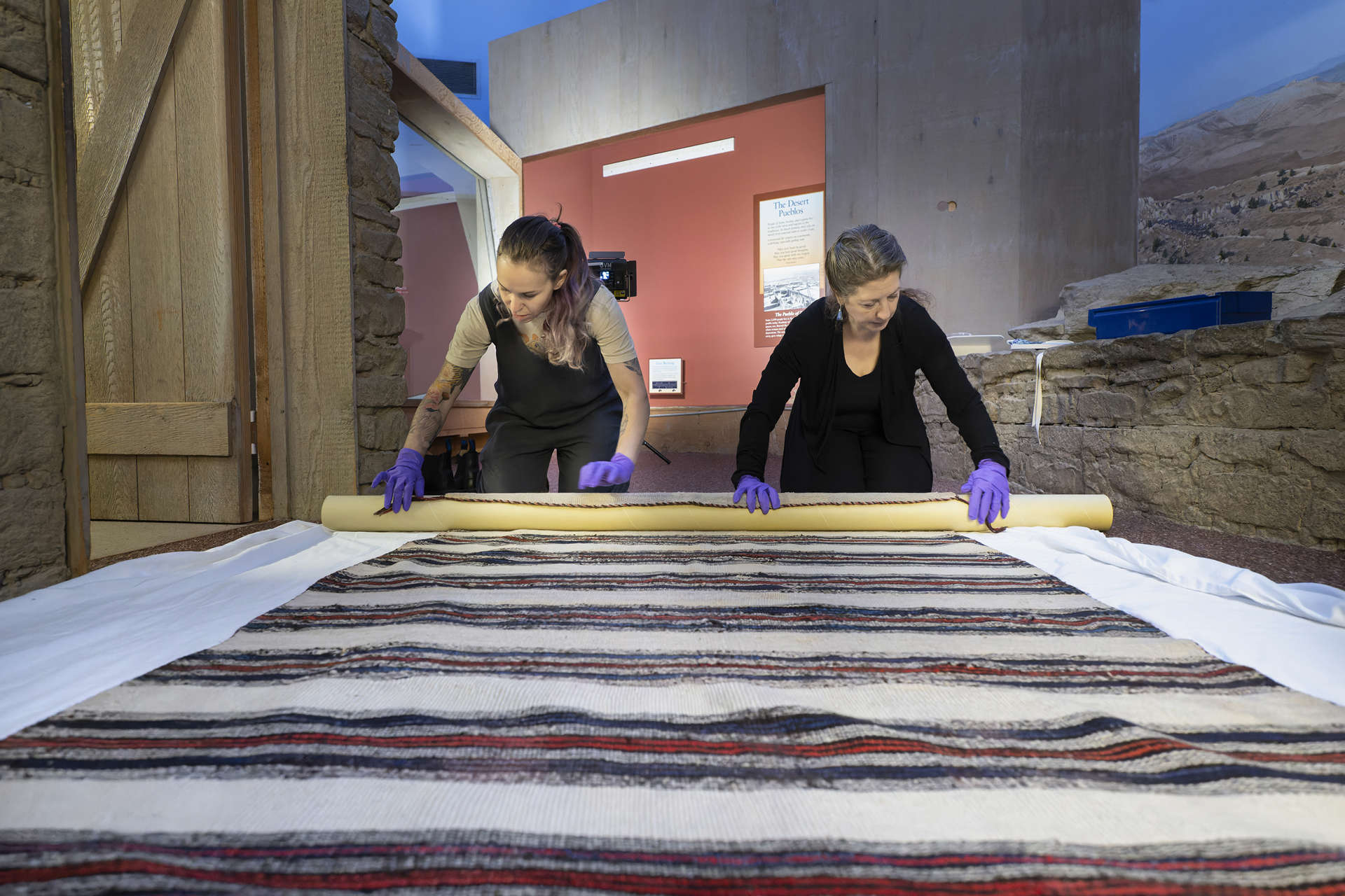 two women roll up a textile
