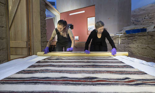 two women roll up a textile