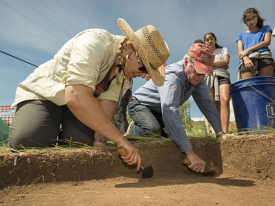 Curator Michele Koons in the foreground with another volunteer using a trowel to scrape another level of dirt from the site