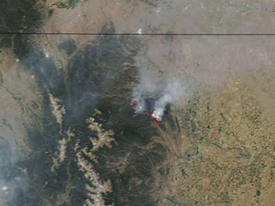 Aerial view of Colorado showing at least two large forest fires in the mountains, clearly showing smoke covering much of the state