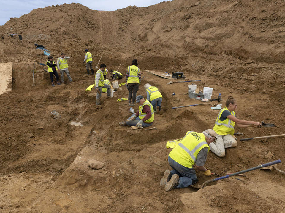 a wide view of a large excavated dirt area with a group of people working in it.