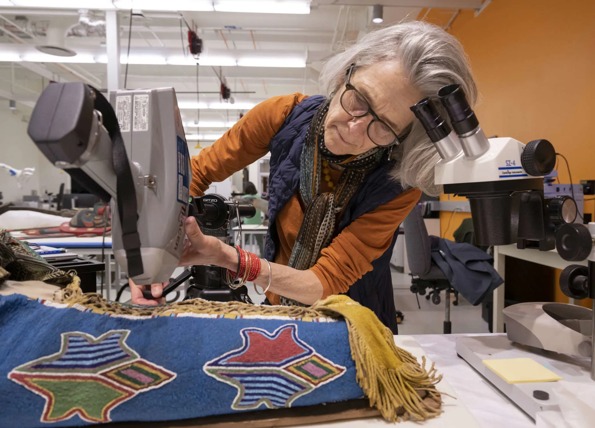Woman holding an X-Ray Fluorescence spectrometer against a beaded cradleboard to identify elements present. 