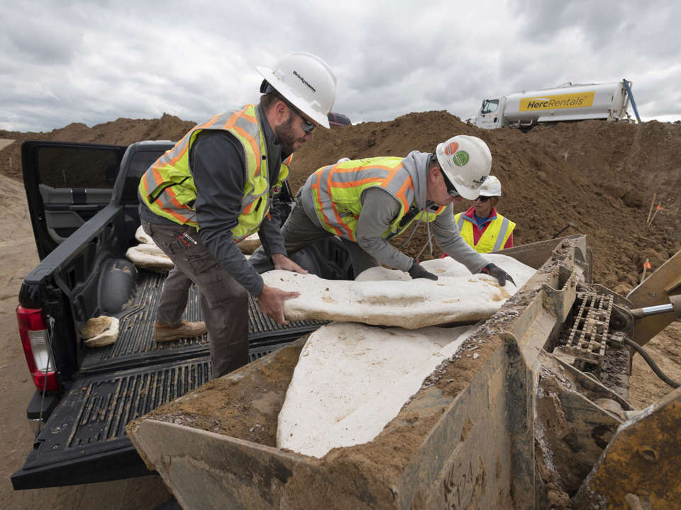 Two people in hard hats adding white field jackets to construction equipment from the bed of a truck