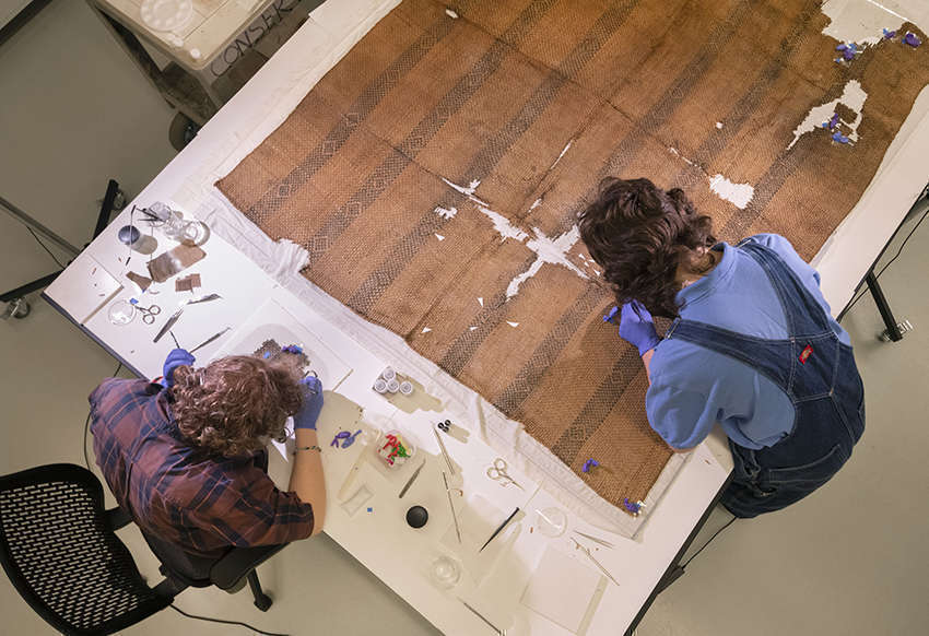 Overhead view of two staff working to conserve a damaged textile