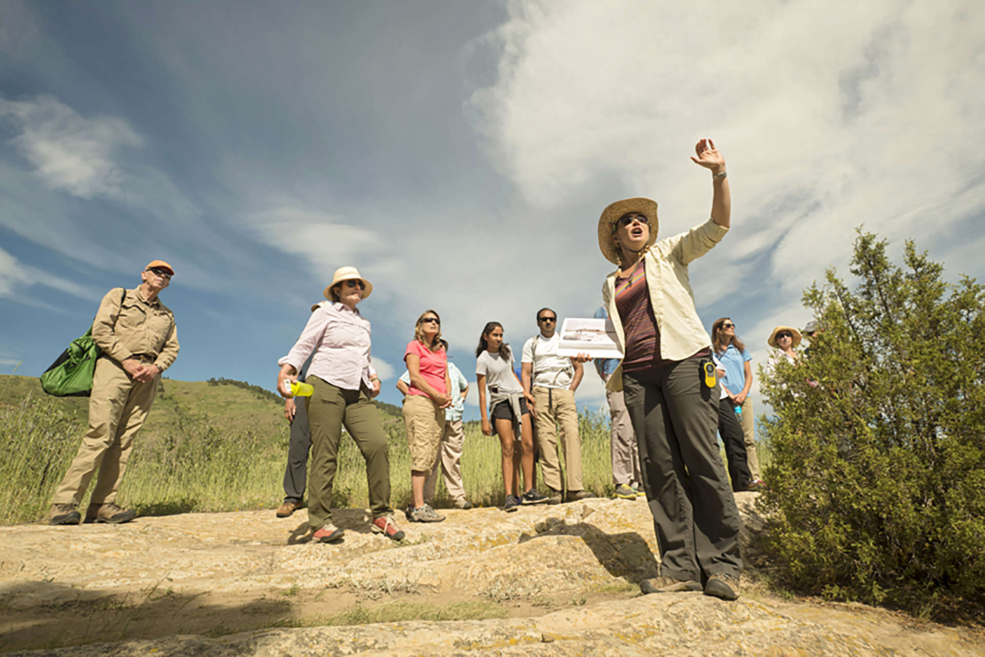 A group stands on a trail in a field listening to Michele Koons talk about the history of the Magic Mountain site.